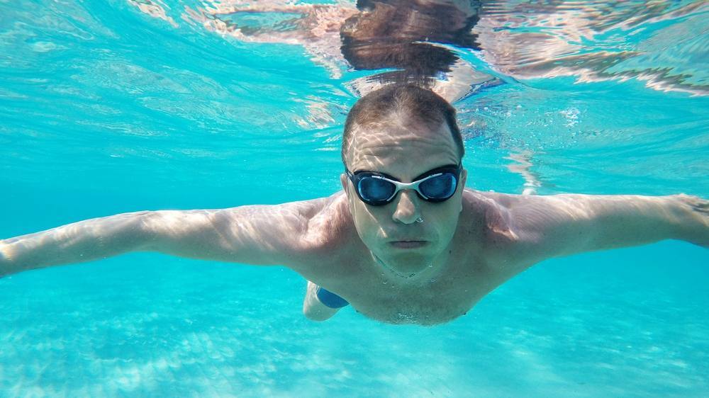 رجل يرتدي النظارات الواقية من الماء ويسبح تحت الماء في حمام سباحة