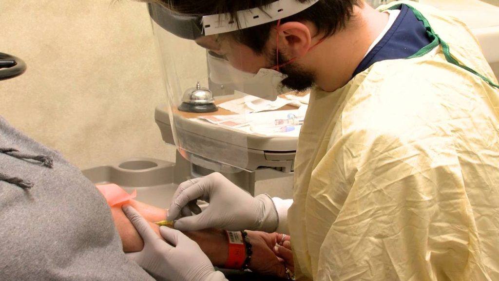 ممرض مايو كلينك، رجل يرتدي معدات الوقاية الشخصية بما في ذلك واقي الوجه، خلال تقديم العلاج بالأجسام المضادة أحادية النسيلة خلال فيروس كورونا المستجد (كوفيد-19)