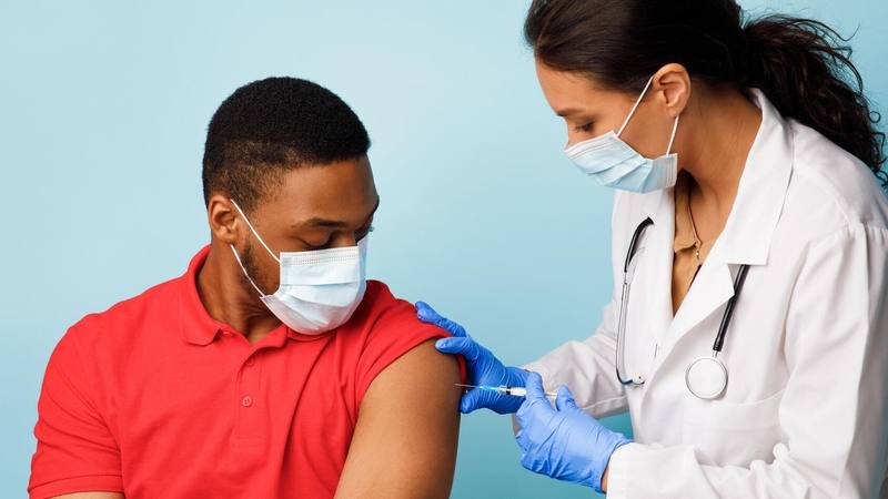 Jovem negro recebendo vacina de uma profissional de saúde