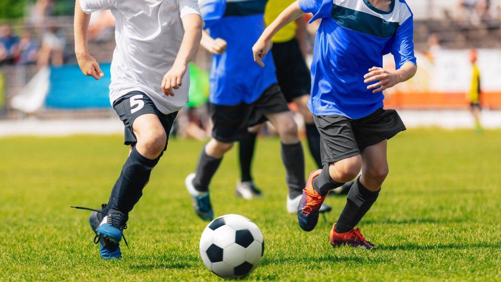 um grupo de adolescentes em uniformes azul e branco jogando futebol em um campo verde