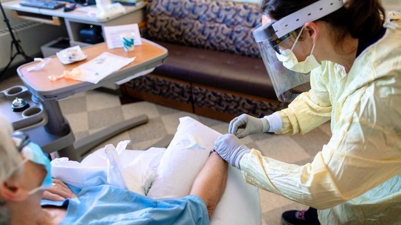 uma médica da Mayo Clinic, uma jovem mulher, com EPI completo preparando um paciente para transfusão de anticorpo monoclonal
