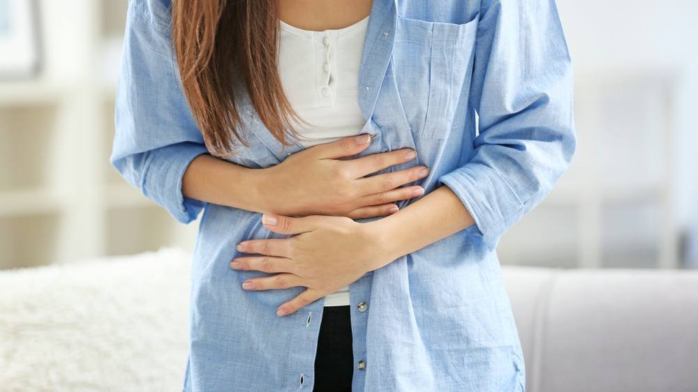 uma jovem mulher curvada segurando o estômago com dor, talvez com cólicas abdominais ou menstruais