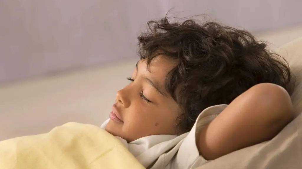 uma criança com cabelo escuro encaracolado dormindo em um travesseiro
