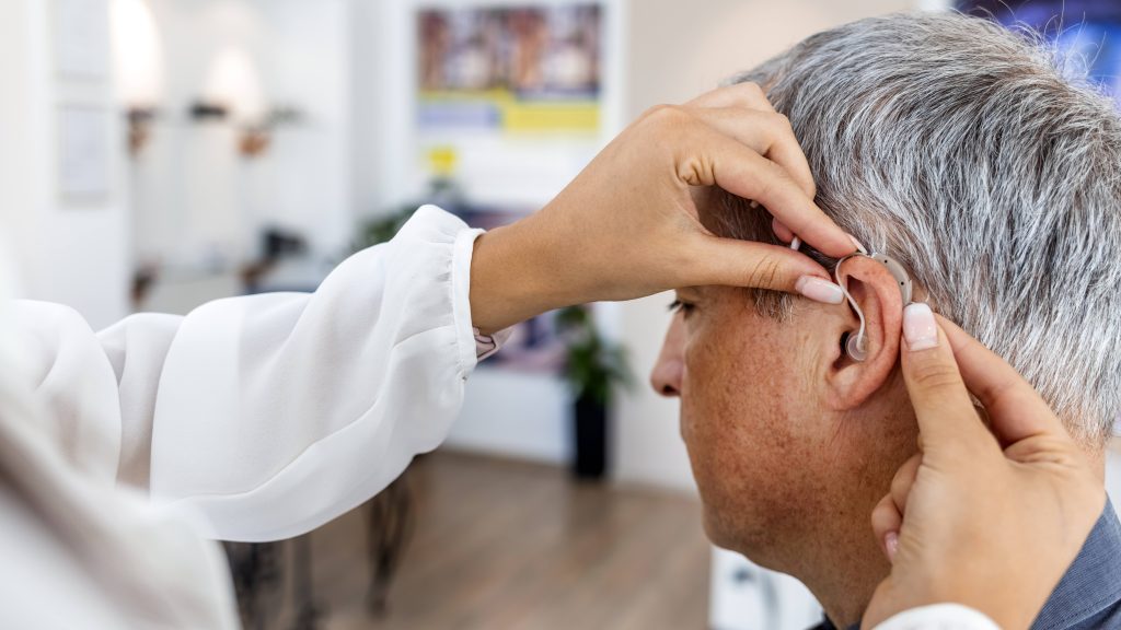 Médico colocando um aparelho auditivo no ouvido de um paciente homem adulto