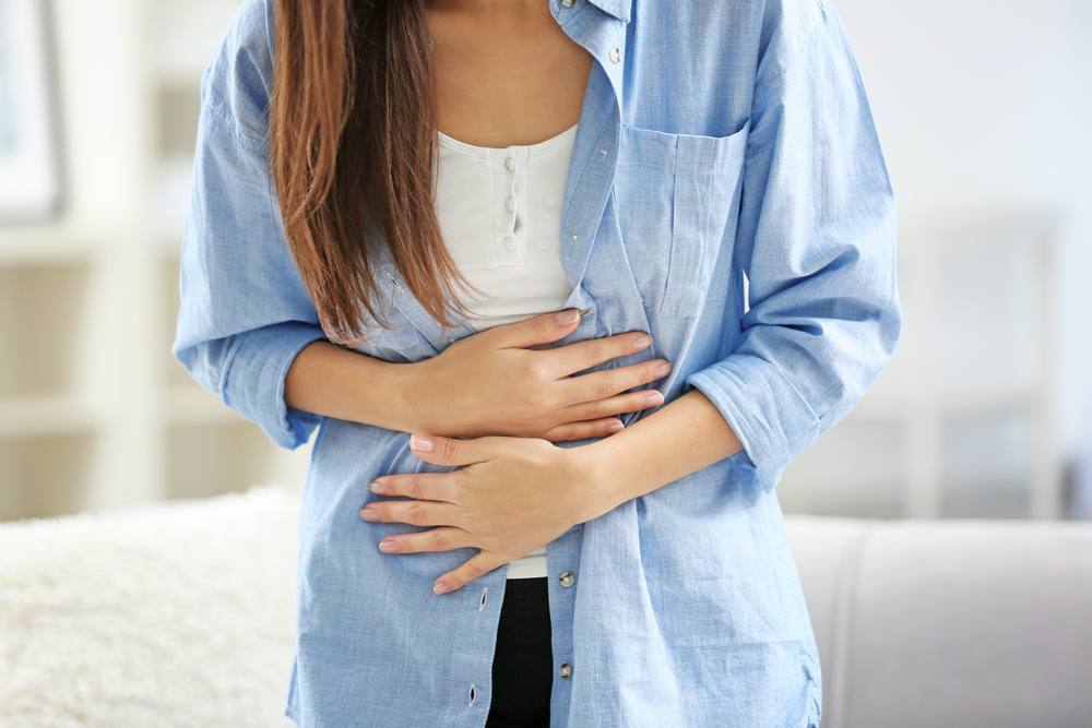 a young woman bending over and holding her stomach in pain, maybe abdominal or menstrual cramps