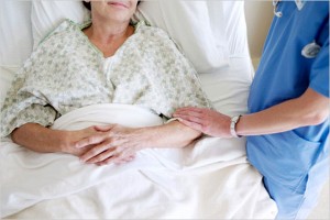 Hospital bed with patient and care giver touching her arm