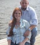 Jessica and her husband standing outside on pier with water in the background 