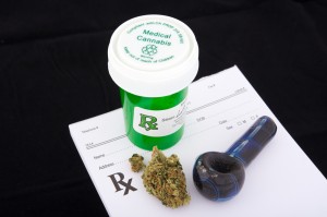 A vial labeled medical cannibis, some marijuana and a small pipe on a prescription pad. 