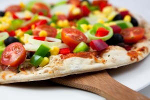 Veggie pizza with red tomatoes and green peppers on a wooden cutting board