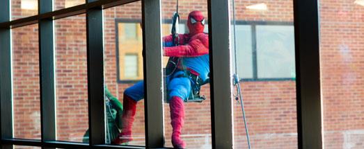 Window washer in Spiderman costume cleaning large hospital window