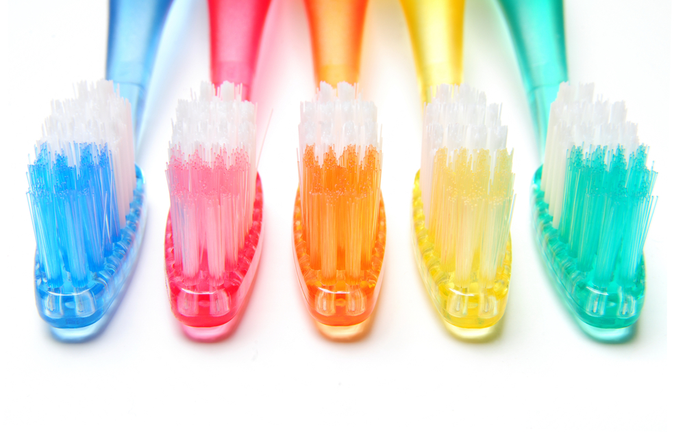 Row of five different colored toothbrushes, blue, pink, orange, yellow and green