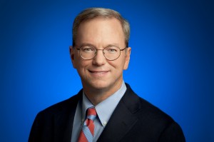 Medium shot of Eric Schmidt wearing glasses in dark suit and red striped tie with blue background