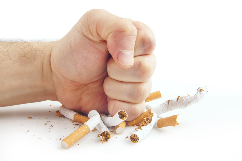 Caucasian man's fist pounding down on a pile of broken cigarettes