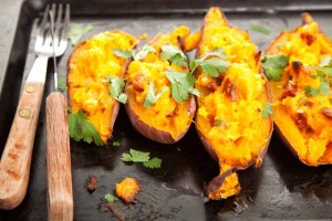 stuffed sweet potatoes cut in half on cooking tray with fork and knife on the side