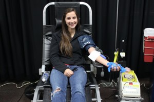 Young woman in jeans and dark sweatshirt on donor bench, donating blood