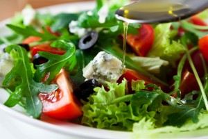 Closeup of Mediterranean diet lettuce salad with sliced tomatoes feta cheese and olive oil dripping from a spoon