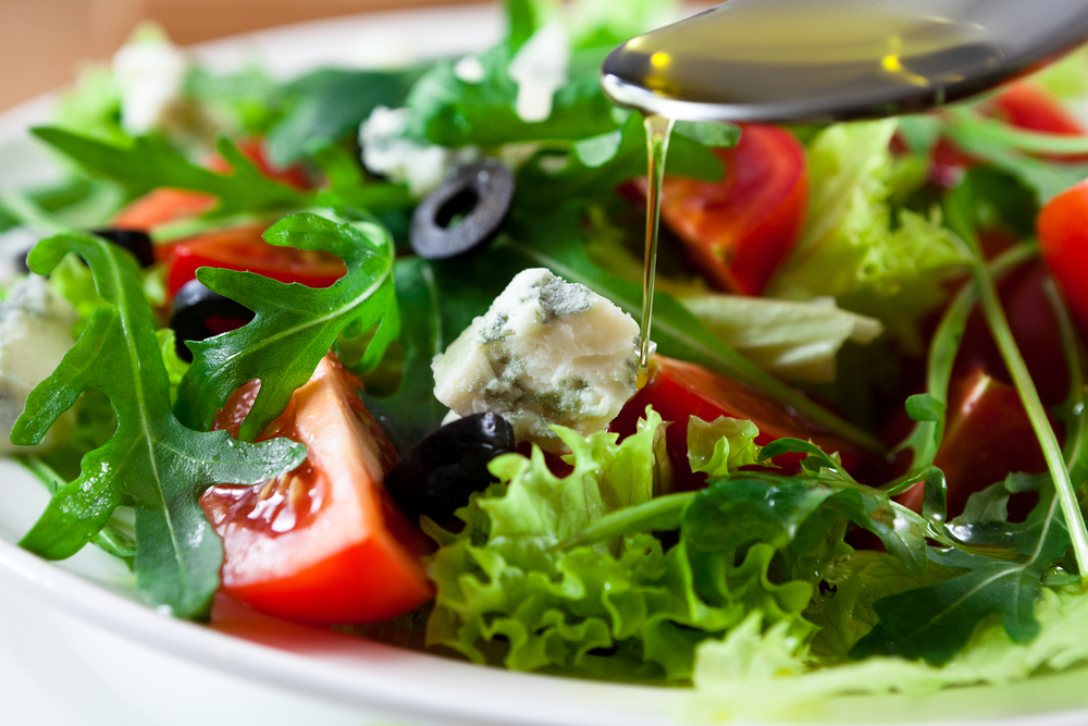 Ensalada mediterránea con aceitunas negras, queso y tomates muy rojos, rociada por aceite de oliva con una cuchara
