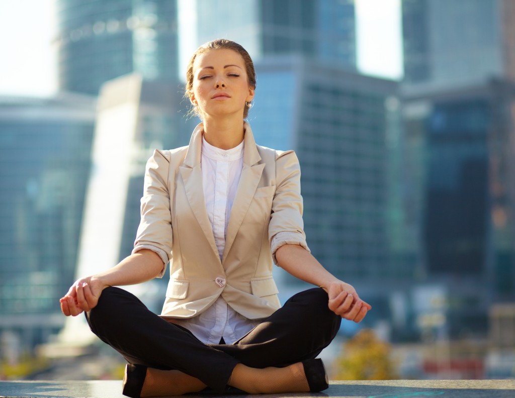 Caucasian business woman meditating with the city skyscrapers in the background