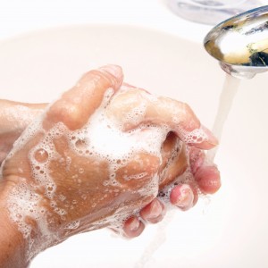 Two caucasian hands washing with soapsuds under a silver water spicket