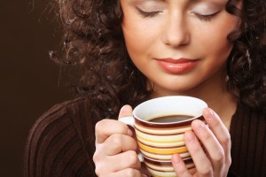 Woman holding cup of coffee with both hands and eyes closed.