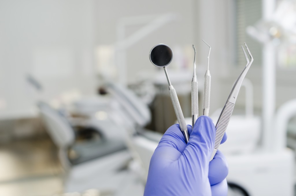 gloved hand holding dental tools to exam teeth