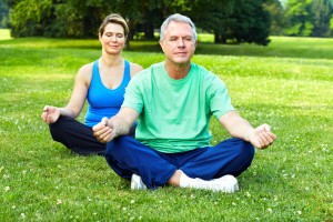 middle-aged couple doing yoga outside on a grassy lawn