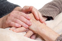 La persona que cuida del paciente le sostiene las manos