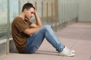 Muchacho adolescente con apariencia triste, sentado en el suelo con la mano en la cabeza