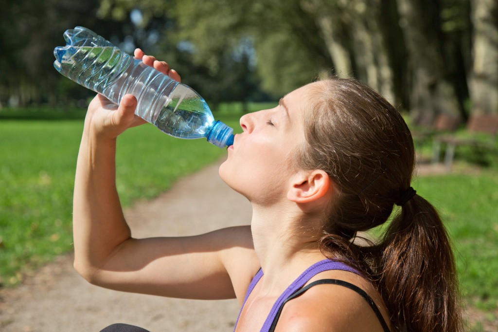 woman drinking out of a water bottle after exercising - staying hydrated
