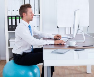 man sitting at work desk on a fitness exercise ball