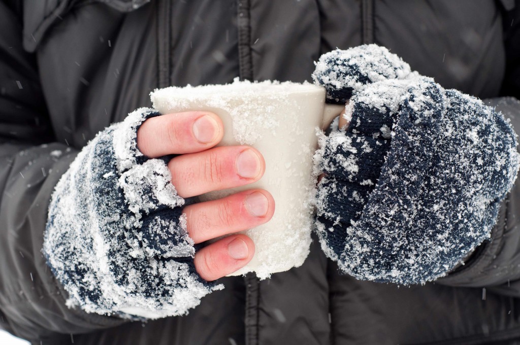 closeup of frozen hands covered in snow holding a cup
