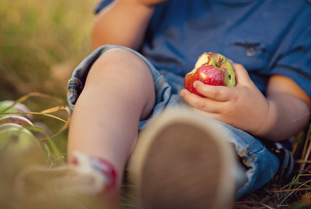 young child sitting on the ground and eating an apple, healthy eating