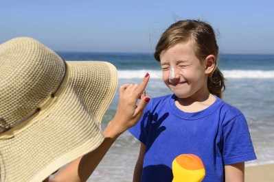 Niña pequeña se asolea en la playa y una persona adulta le aplica protector solar en la nariz