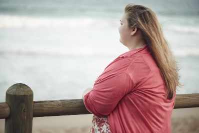 Mujer joven con exceso de peso mira pensativa el mar