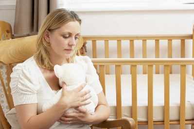 Mujer triste sentada frente a una cuna vacía en la sala de recién nacidos