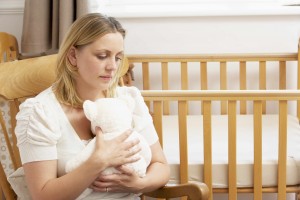 sad young woman sitting by empty crib in baby nursery, miscarriage