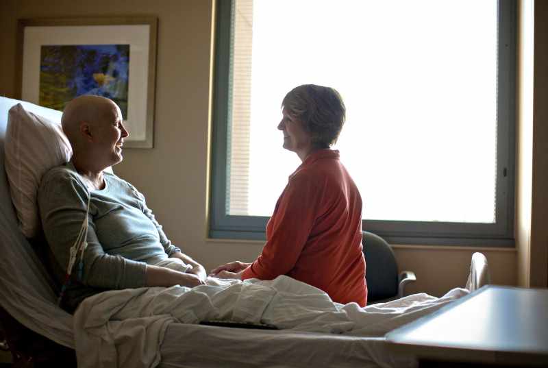 cancer patient in hospital bed talking with friendly visitor