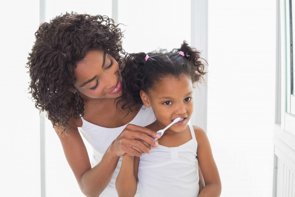 woman helping little girl brush her teeth for dental health