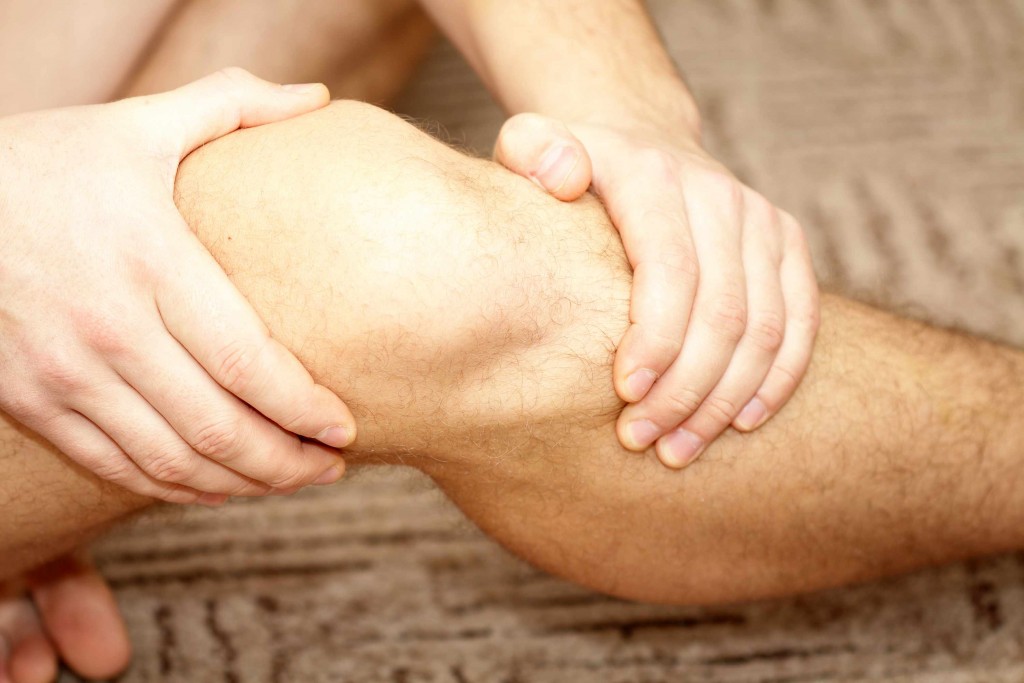 a close-up of a man's knee, with his hands gripping on either side above and below, holding it as though in pain
