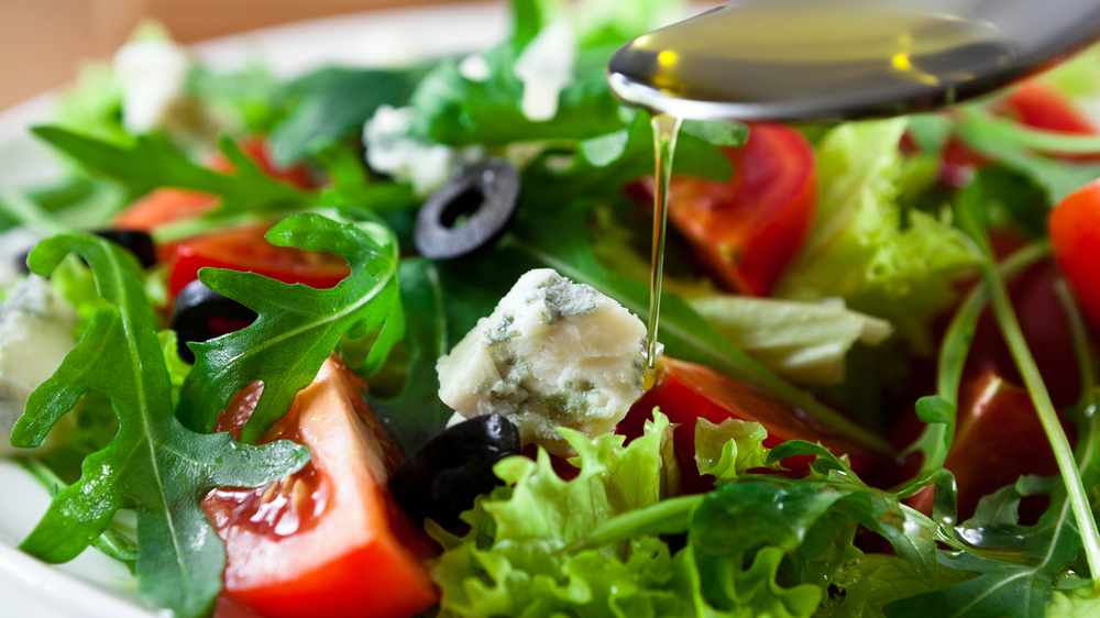 Mediterranean salad with black olives, cheese, bright red tomatoes with olive oil dripping from a spoon 