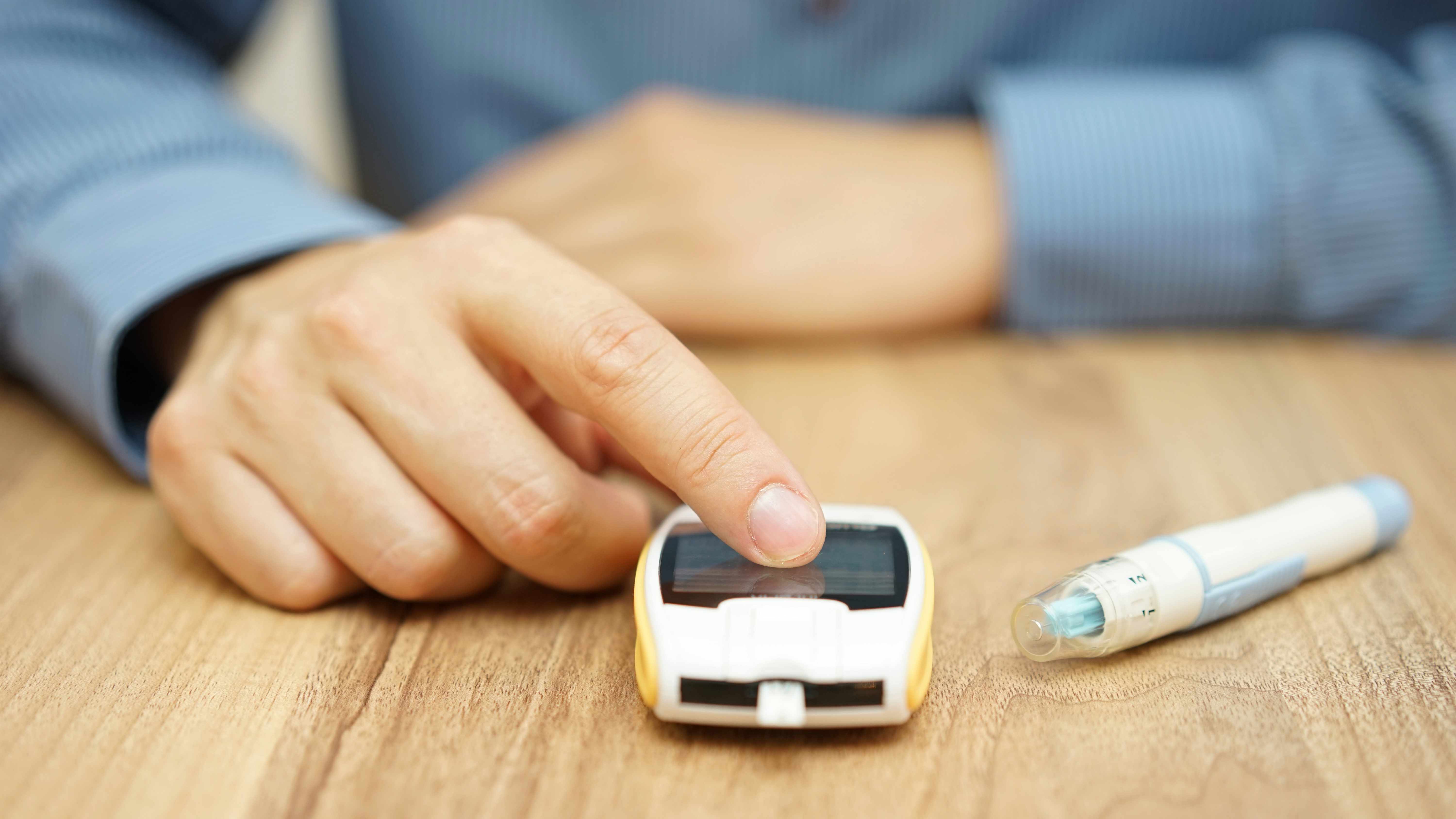 a close-up of a woman's hand with a glucose monitor and lancet on a table