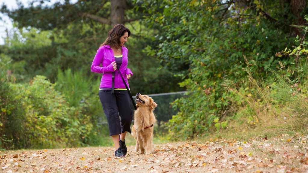 Una mujer hace ejercicio al caminar afuera con su perro