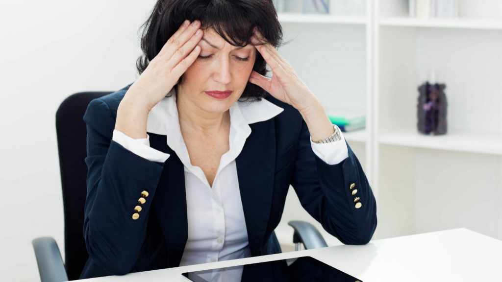 Mujer de negocios de mediana edad en un escritorio con dolor de cabeza
