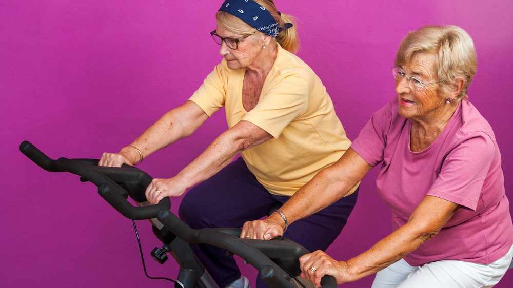 Portrait of two Elderly women doing leg exercises on stationary bikes in gym