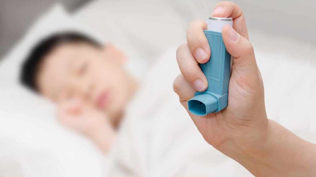 young child sleeping, adult hand holding an inhaler for asthma