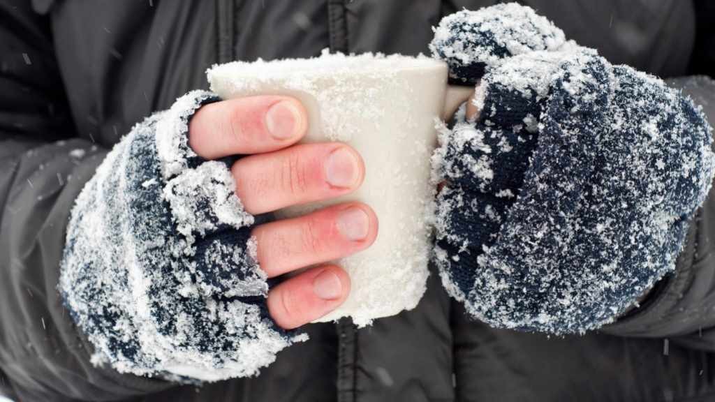 closeup of frozen hands covered in snow holding a cup, frostbite