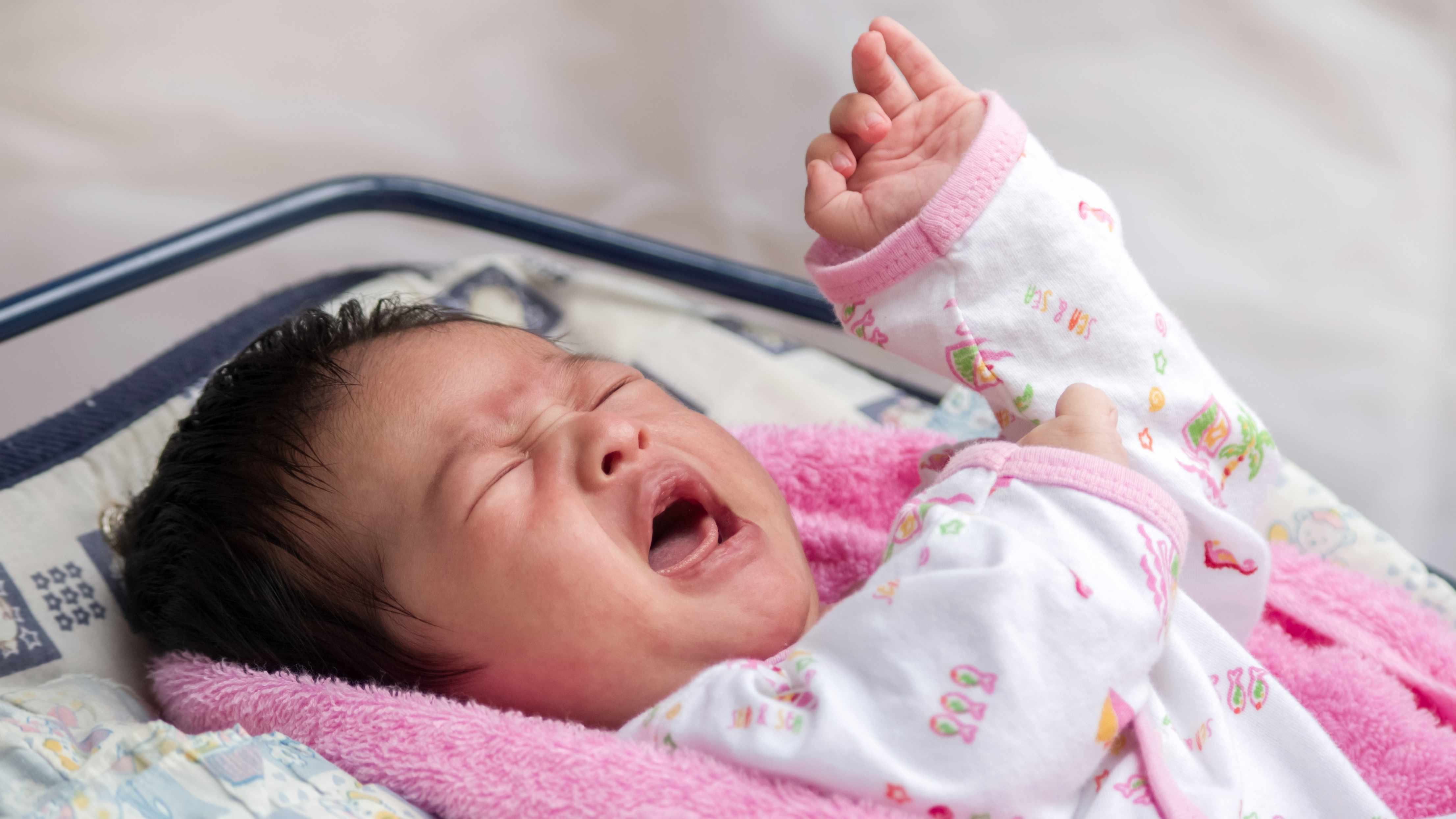 Un bebé triste o enfermo y envuelto en una manta color rosa llora y tose 