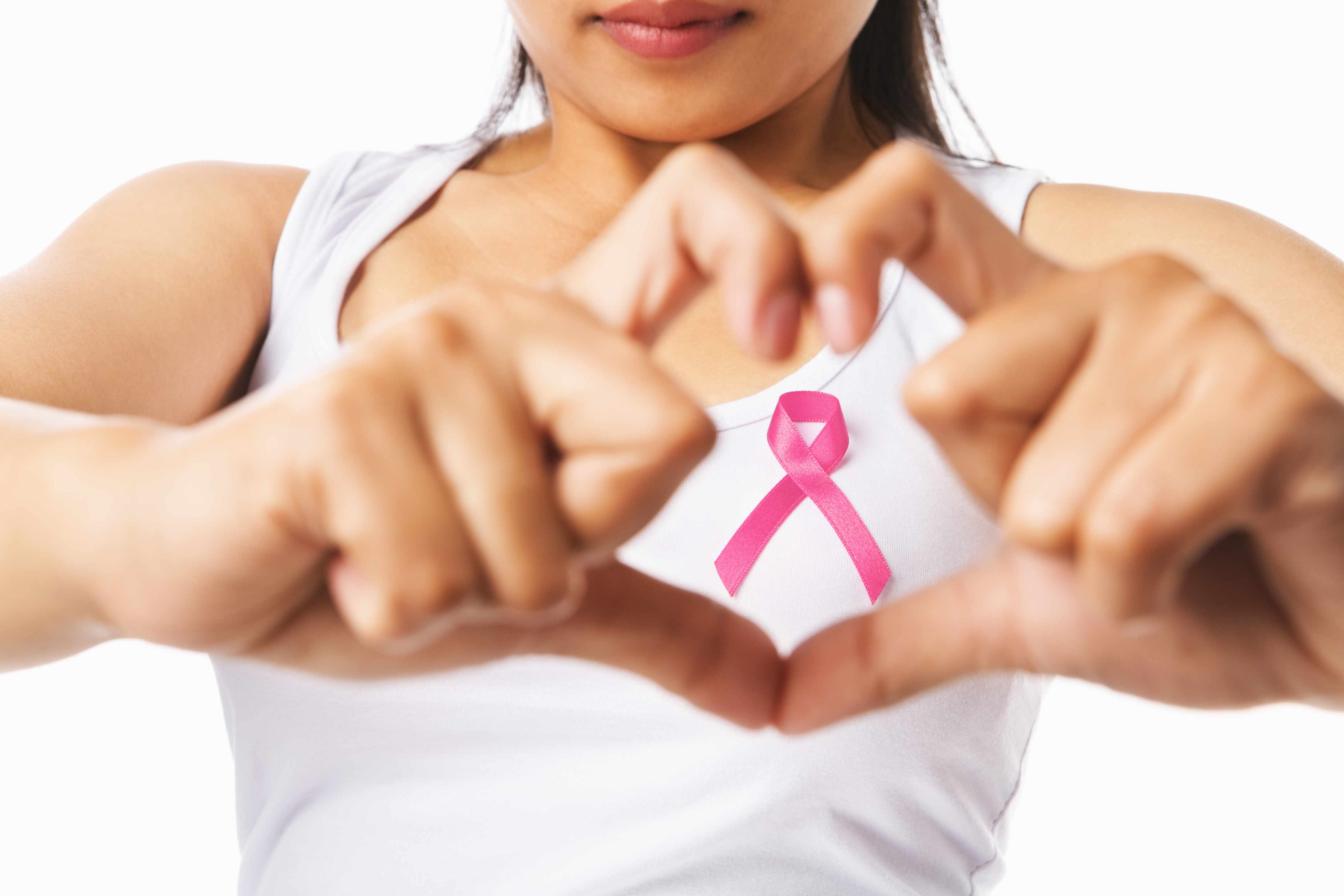 woman in tshirt making heart symbol with hands and pink ribbon, representing breast health