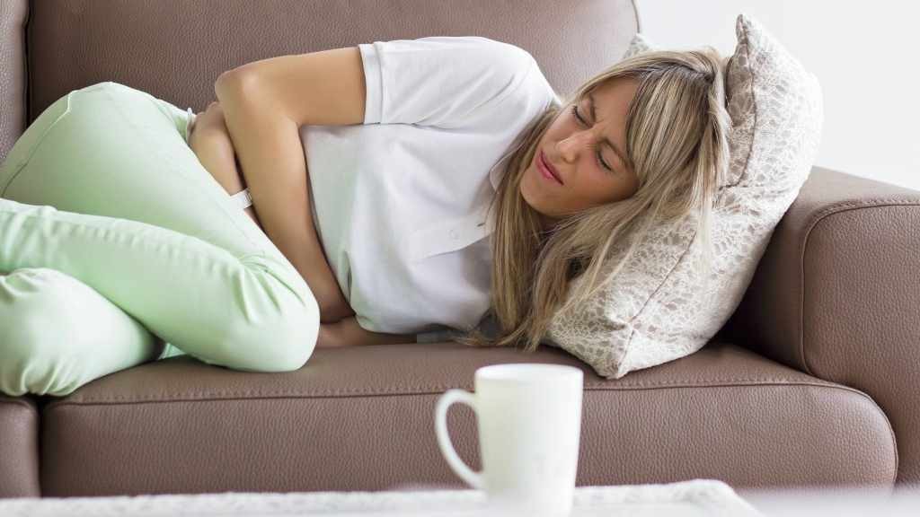 Una mujer sentada en un sofá con cólicos menstruales o dolor de estómago
