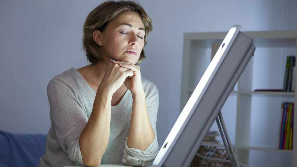 Mujer sentada junto a la lámpara de la terapia de luz para el trastorno afectivo estacional o la depresión